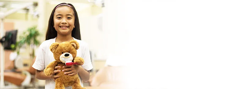 A girl holding a teddy bear with a toothbrush.