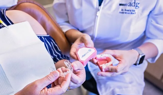 A dentist holding Invisalign aligners and a container.