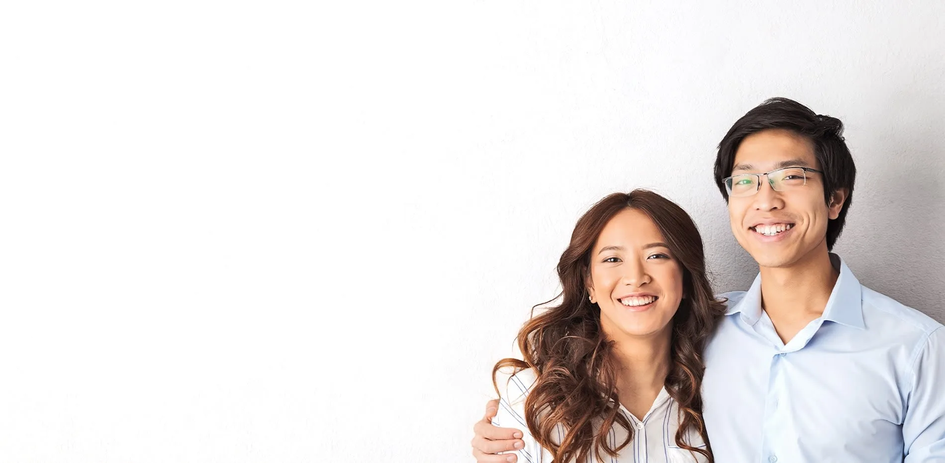 A smiling couple posing together against a white wall.
