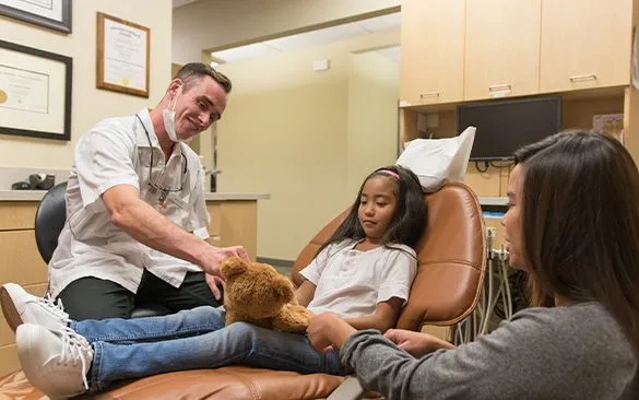 A dentist with a young girl and her guardian in a dental office.