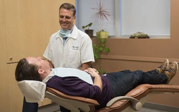 A dentist smiling at a reclining patient in a dental clinic.