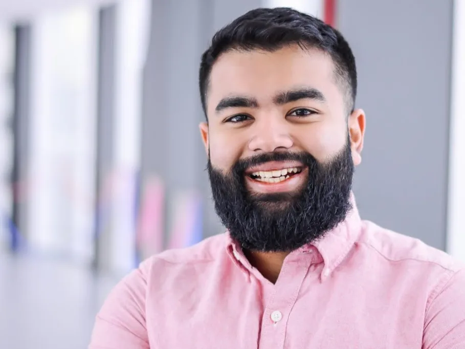 A smiling man in a pink shirt with a beard.