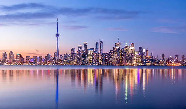 Toronto skyline at dusk with reflected lights in the water.