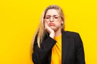 A woman in a blazer looking thoughtful against a yellow background.