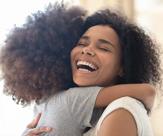 A woman happily hugging a child with curly hair.