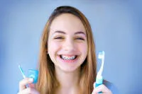 A girl with braces smiling while holding a toothbrush and mouthwash cup.