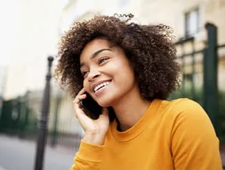 A young woman smiling and talking on a phone outdoors.