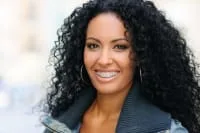 A woman with curly hair and braces smiles at the camera.