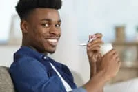 A young man smiling while holding a spoon and cup.