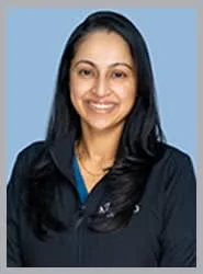 A smiling female dentist in a black jacket and blue scrubs.