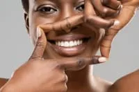 A woman smiles while framing her face with her hands.