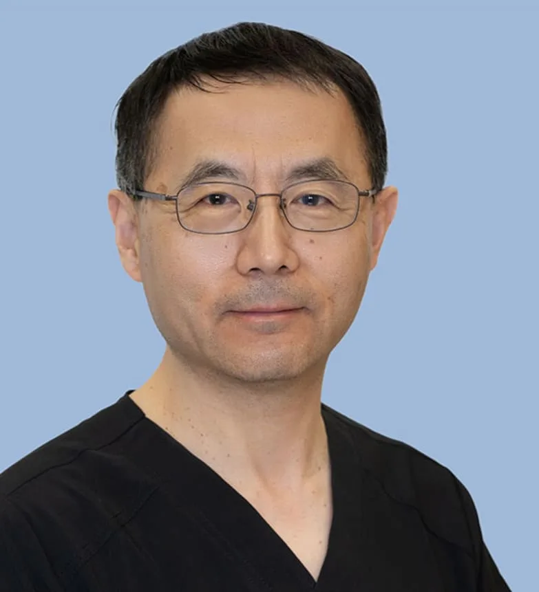 A dental professional in a black scrub top against a light blue background.