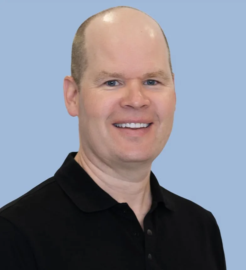 A smiling dentist in a black polo shirt.