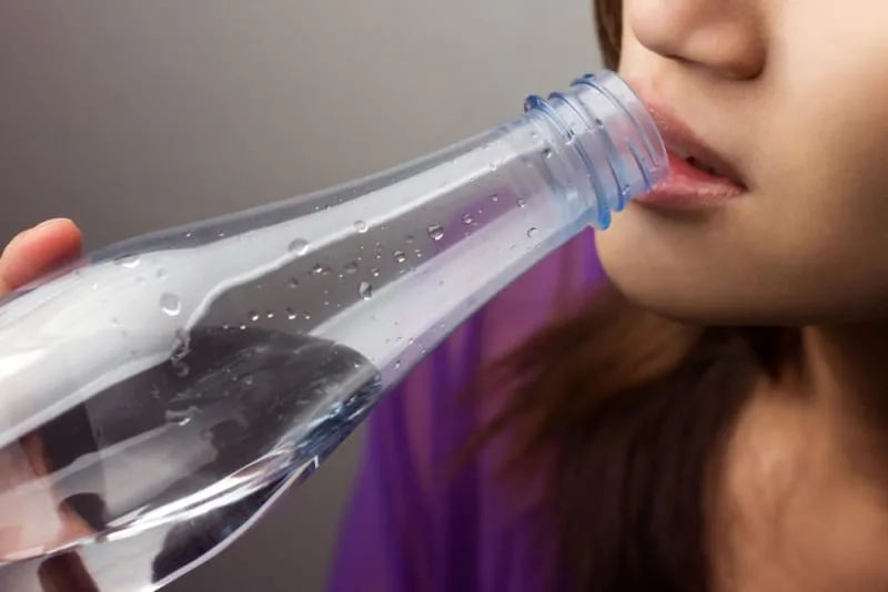 A woman drinking from a clear water bottle.