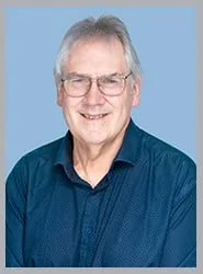 A smiling senior man in a blue shirt with glasses.