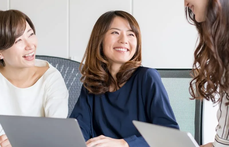 Three women discussing in a modern office setting.