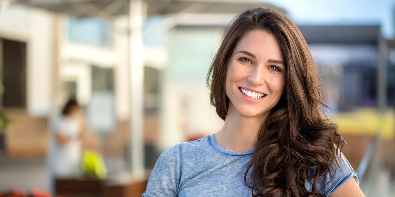 Happy young woman smiling outdoors in a blue shirt.