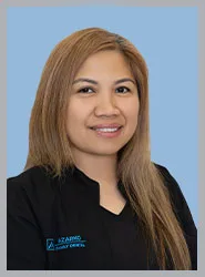 Dental professional smiling in a black coat against blue background.