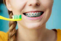A person with braces smiles while holding a toothbrush.