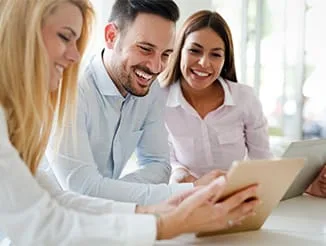 Three adults discussing while using tablets in a bright setting.