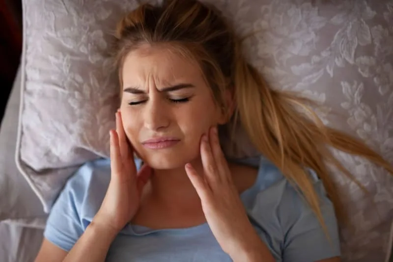 A woman lying down holding her jaw in pain.