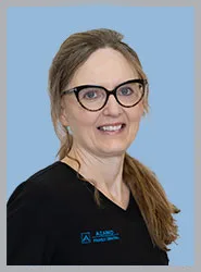 A woman in scrubs smiling against a light blue background.