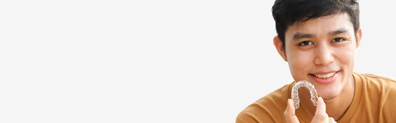 A young man holding a clear Invisalign aligner.