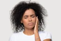 Woman expressing dental pain while holding her cheek.