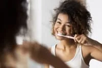 A young woman brushing her teeth in front of a mirror.