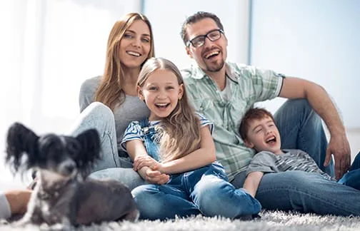 A smiling family with a dog sitting on a rug.