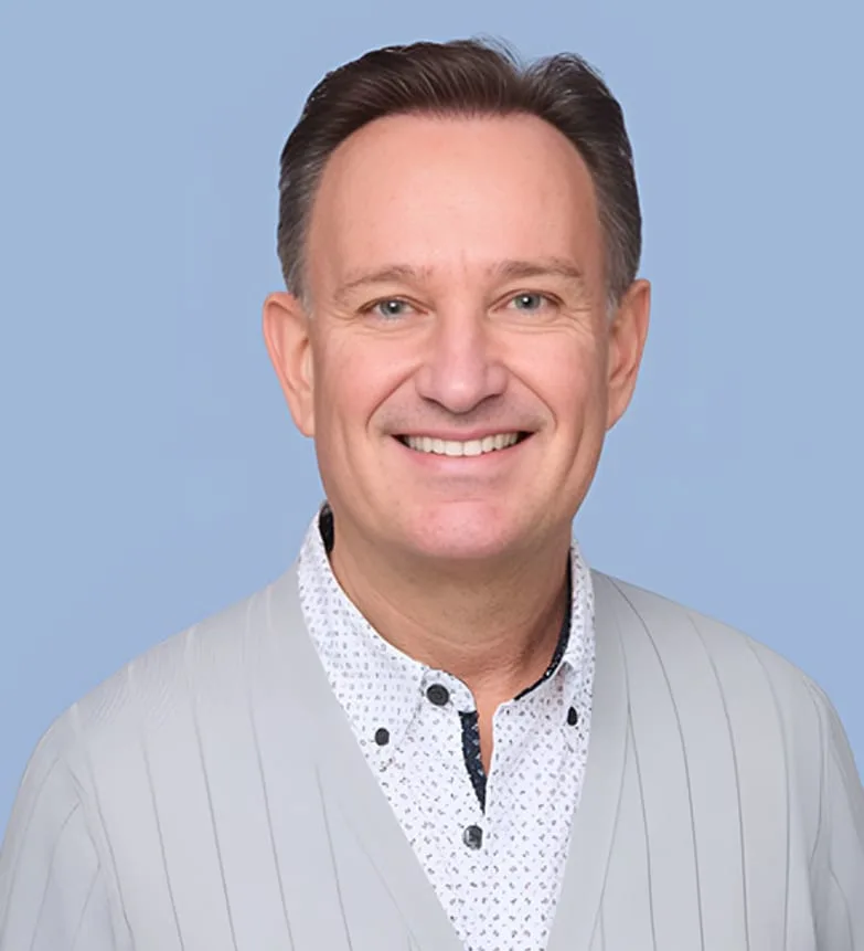 A smiling man in a gray sweater against a blue background.
