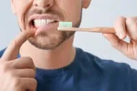 A person brushing their teeth with a bamboo toothbrush.