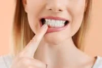 A woman pointing at her white teeth and smiling.