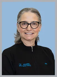 A smiling woman in a black dental jacket with glasses.