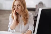 Woman sitting at a desk with a pained expression.