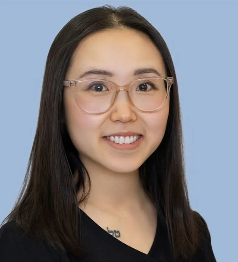A smiling woman with glasses and dark hair in a blue background.