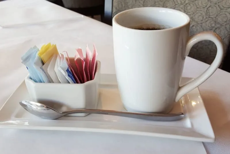 A white coffee mug with sugar packets on a plate.