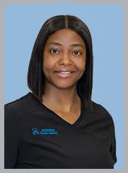 A smiling woman in dental scrubs with black hair.