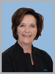 A smiling woman in a dental uniform with a blue background.