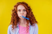 Young woman with curly hair holding a toothbrush in her mouth.