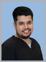 A smiling male dentist in a black scrub with a blue background.