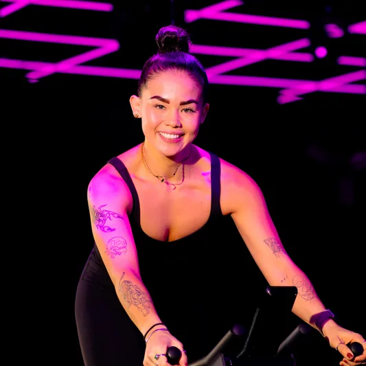 A woman cycling in a fitness class with purple lighting.