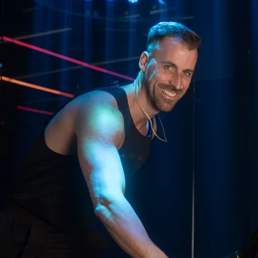 A smiling man in fitness attire with colorful studio lights.