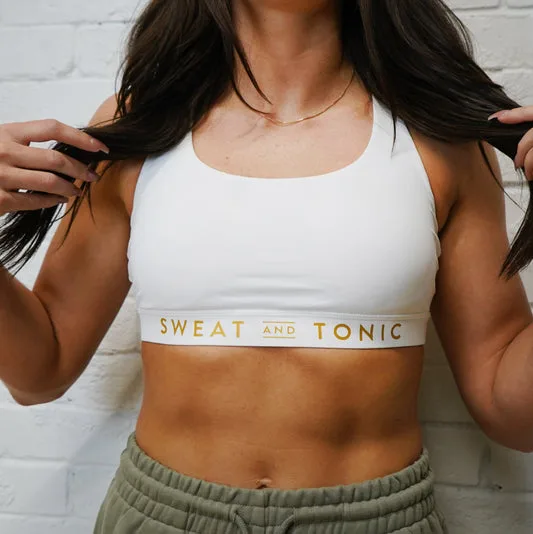A woman models a white sports bra with gold lettering.
