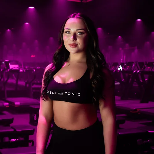 A woman in fitness attire stands in a gym with purple lighting.