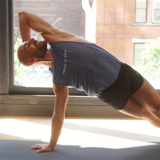 A man demonstrating a side plank exercise in a fitness studio.