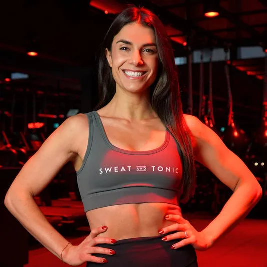 A fitness instructor in a grey crop top smiling in a studio.