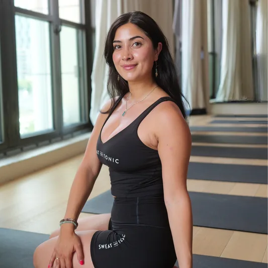 A woman seated in a yoga studio wearing fitness attire.