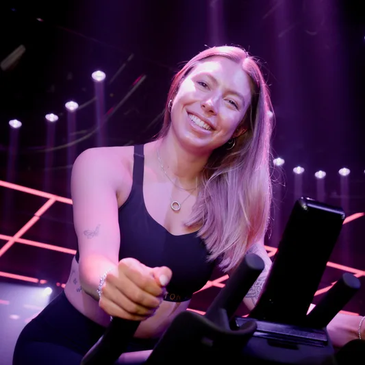 A smiling woman cycling in a modern fitness studio.