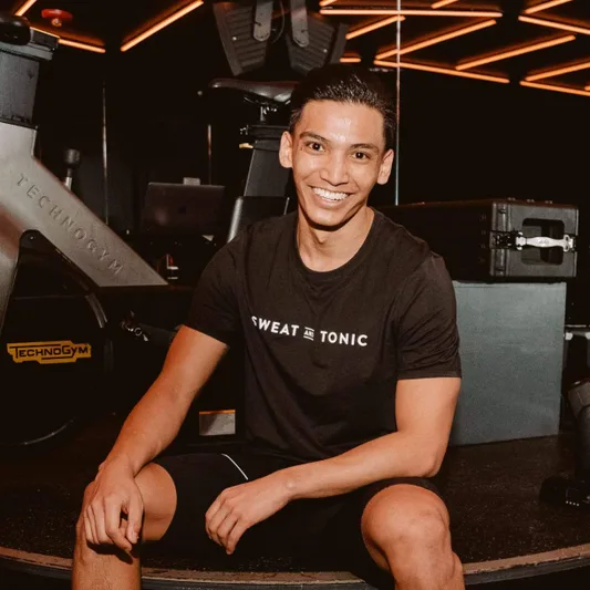 A smiling person in a gym setting wearing a Sweat and Tonic t-shirt.